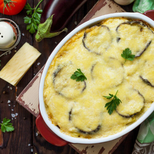 Eggplant casserole with beshamel (moussaka) - a traditional Greek dish on the kitchen wooden background. Top view flat lay background.